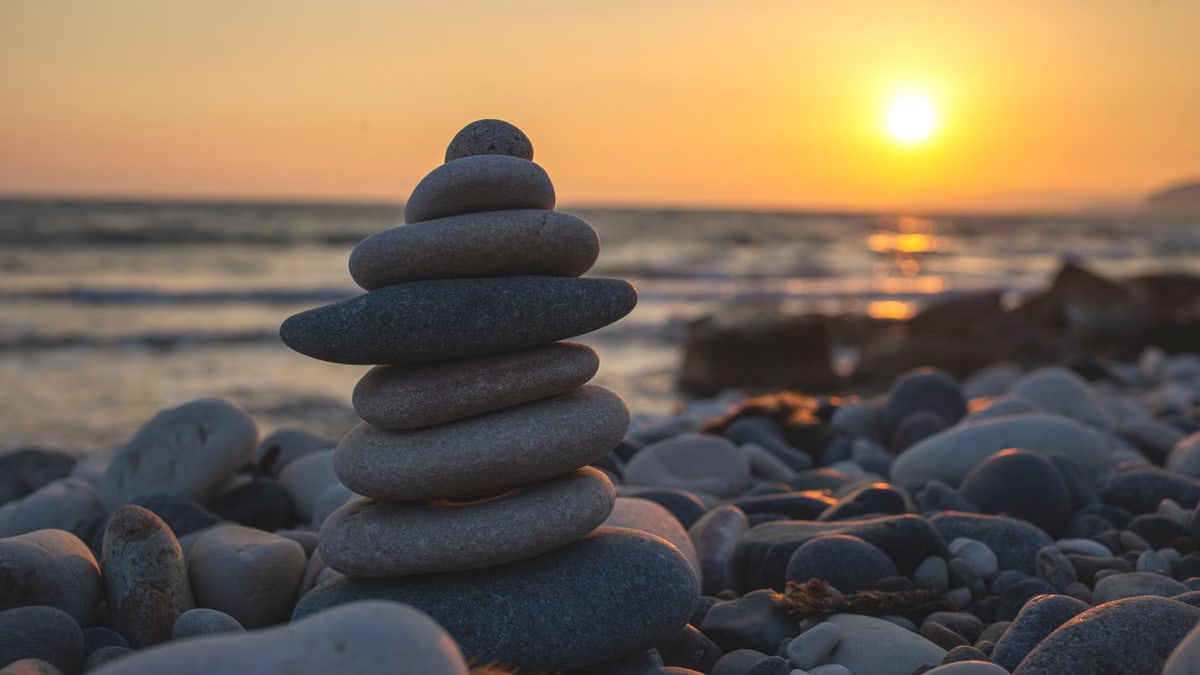 Tranquil sunset at the beach with stacked stone cairn and golden hour light, perfect for relaxation themes.