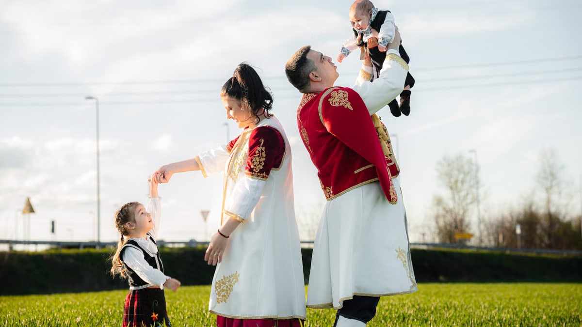 A family of four in traditional attire enjoying a sunny day outdoors, with parents holding children.